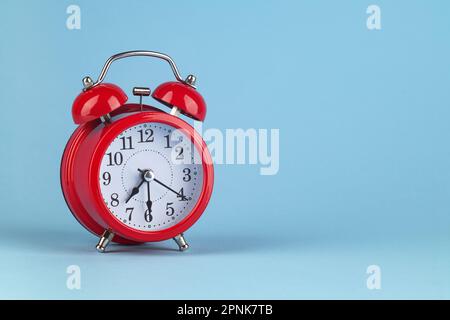 Red alarm clock on a light blue background. It's 7:30 o'clock on the clock. Morning. Place for text. Stock Photo