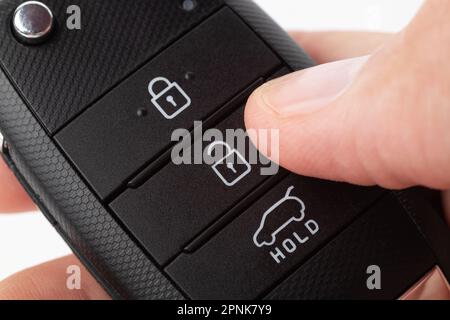 Unlocking a car with button on the keychain. Man's hand holds car key on white background close up. Stock Photo