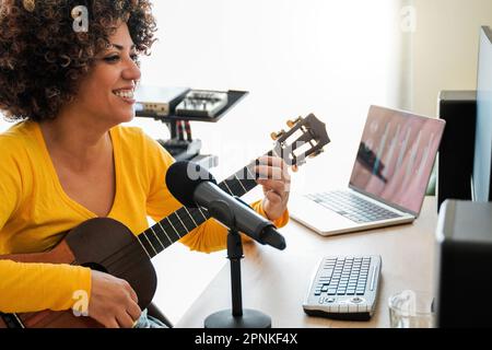 African musician insdie music home studio recording ukulele guitar song - Audio engineer woman mixing album - Soft focus on woman face Stock Photo