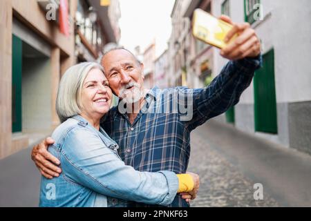 Happy senior couple taking selfie with mobile phone outdoor - Elderly tourist and travel vacations - Focus on faces Stock Photo