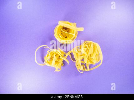 three pasta nests of tagliatelle isolated on a purple background Stock Photo