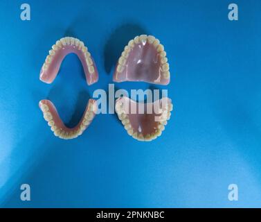 two pair of Dentures (top and bottom) - removable false teeth made of acrylic isolated on a blue background - both sets facing up Stock Photo