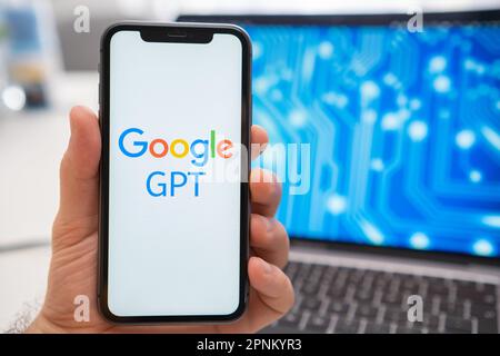 A man is holding a smartphone with a Google GPT neural network logo on the screen, while in the background, a laptop displays a neuronet on the splash screen. March 2023, Prague, Czech Republic  Stock Photo