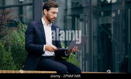 Professional consultant businessman sits outdoors communicating via video call on laptop consulting client at online conference talking via webcam Stock Photo
