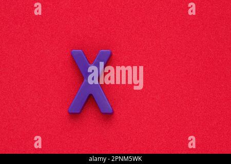 Alphabet letter X - Violet colored plastic piece on red 032 c foamy background Stock Photo