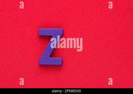 Alphabet letter Z - Violet colored plastic piece on red 032 c foamy background Stock Photo