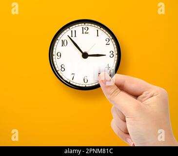 Hand holding small clock on yellow background Stock Photo