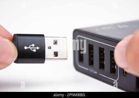 USB A charging cable in hand is plugging into a multi port mobile phone charger. Stock Photo