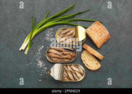 Opened tin cans with sprats in oil, green onion and bread on black table Stock Photo