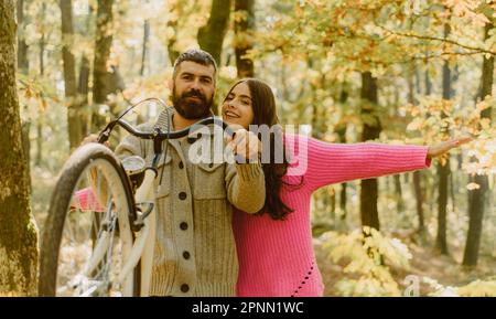 The young couple taking the bike and running away from the office work. Wearing knitted sweaters. Walking together, having pleasant smiles on faces Stock Photo