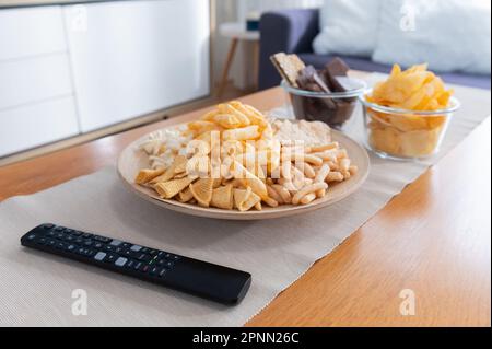 Snack on a wooden table and a TV remote control Stock Photo