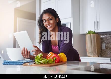 My digital sous chef. a young woman using a digital tablet while preparing a healthy meal at home. Stock Photo