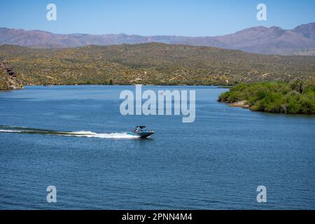 A bright summer day reveals a beautiful reservoir in the mountains, with a small nautical vessel gliding across its calm waters. Stock Photo