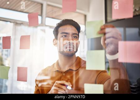 Planning, writing and focused man on glass for project management, workflow and business schedule. Asian person brainstorming ideas, moodboard and Stock Photo