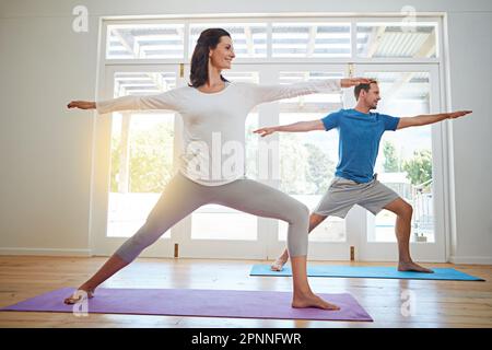 Practicing yoga together. Full length shot of a mature couple practicing yoga in their home. Stock Photo