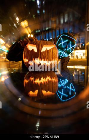 Purge mask, Halloween pumpkin, man in a suit with LED mask. At night, city lights Frankfurt am Main, Hesse, Germany Stock Photo