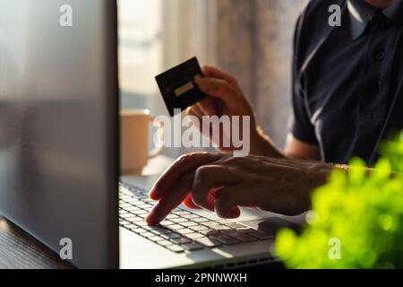 Online shopping. Man hand holding credit card and using laptop at home. E-commerce, internet banking, working from home concept Stock Photo