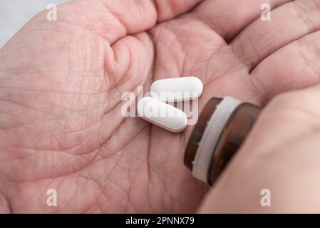 Man taking painkiller white pills on male hand pouring tablets from meds bottle. Taking medicine, health care, pharmacy and treatment concept. Close u Stock Photo