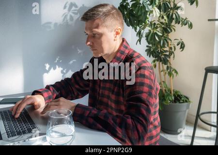 Handsome young man freelancer or IT specialist using a laptop while working in sunny cafe. Male student using computer for distance learning and educa Stock Photo