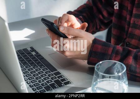 Close up of man hands using smartphone texting message, searching information, browsing. Male freelancer using mobile phone and laptop in cafe Stock Photo
