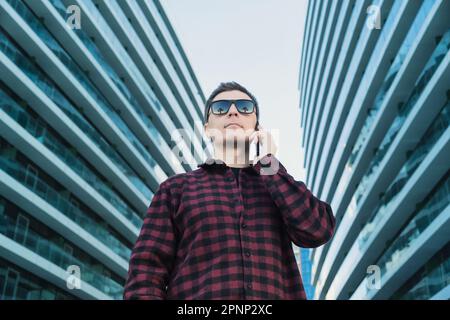 Portrait of IT specialist in sunglasses with palm reflection and using mobile phone or smartphone device outside modern office buildings. Funny shot Stock Photo