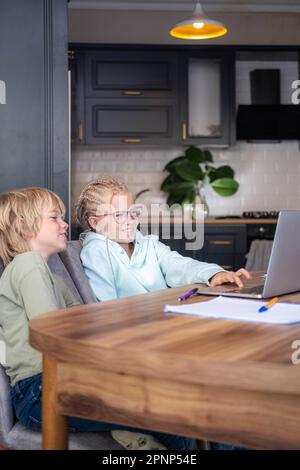 Online school class, siblings pupils boy and girl learning together remotely online at home, looking to laptop, speaking with teacher or tutor using Stock Photo