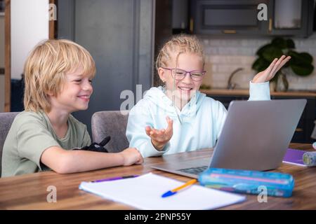 Online school class, siblings pupils boy and girl learning together remotely online at home, looking to laptop, speaking with teacher or tutor using Stock Photo