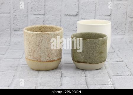 Ceramic cups in different sizes and colors. Ceramic glasses on a gray background. Earthenware covered with matte glaze. ceramic studio. Empty beige wh Stock Photo