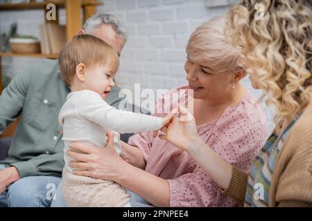 blurred woman touching hand of little daughter while spending time with mature parents in living room,stock image Stock Photo