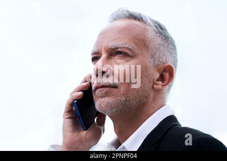 Confident middle aged man using mobile to work, standing outdoors with white background. Stock Photo