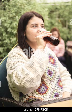Vertical portrait of beautiful brunette woman and new mom looking away drinking a non-alcoholic drink in a beer garden at the pub after a walk Stock Photo