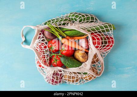 Mesh shopping bag with organic vegetables on blue background. Sustainable lifestyle, zero waste, plastic free concept. Eco friendly shopping Stock Photo
