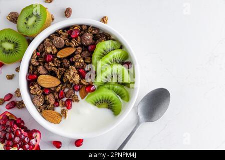 Chocolate oat homemade granola with fresh fruits and berries in a bowl with a spoon on white table. Top view. Healthy breakfast Stock Photo