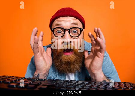 Closeup photo of website developer senior programmer man working late nights code problem stupor near keyboard isolated on orange color background Stock Photo