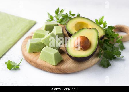 Frozen mashed avocado in portions and a thin layer with fresh avocado and parsley on a light blue background. Seasonal home preparation Stock Photo