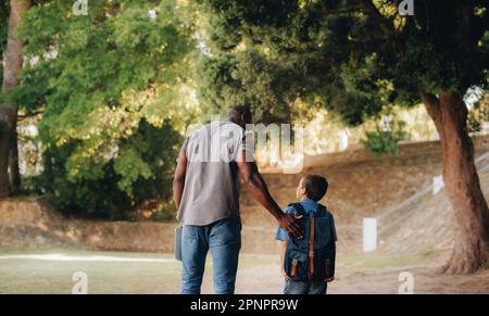 Child mentorship in primary school. Rearview of a male teacher talking and walking with a young school kid outside. Providing support and encouragemen Stock Photo