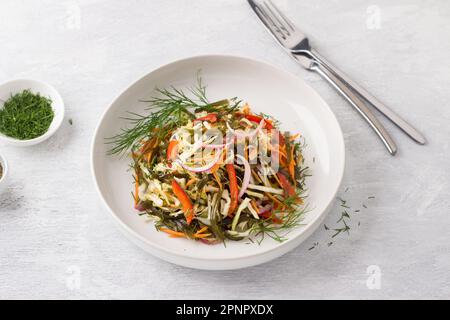 White plate with a salad of seaweed, white cabbage, carrots, sweet peppers, pickled red onions and herbs on a light gray background, top view. Healthy Stock Photo