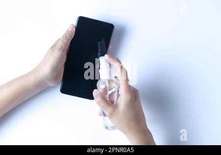 Overhead view of a woman spraying disinfectant on a mobile phone Stock Photo