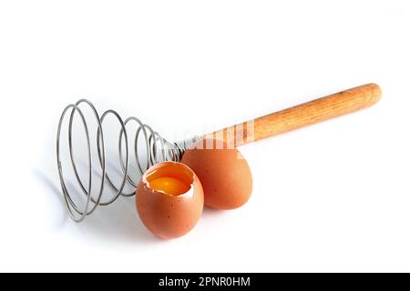 Two beige chicken eggs and a rare beater for beating. Cooking ingredients isolated on white background Stock Photo