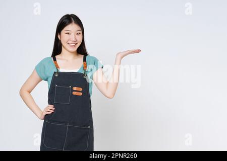 Young woman wearing kitchen apron, presenting or showing open hand palm with copy space for product isolated on white background. Stock Photo