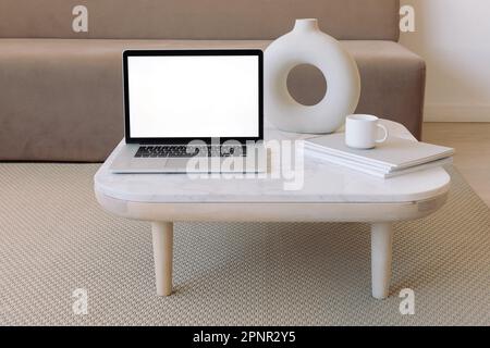 Close-up of an open laptop computer on a coffee table next to a ceramic vase and a cup on a stack of books Stock Photo