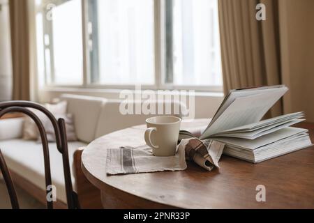 Close-up of an open book, cup and tea towel on a table in a living room Stock Photo