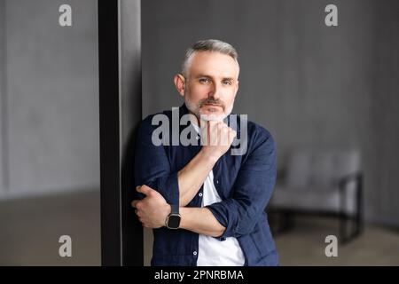 Headshot portrait of attractive man with toothy smile looking at camera at modern living room. Stock Photo