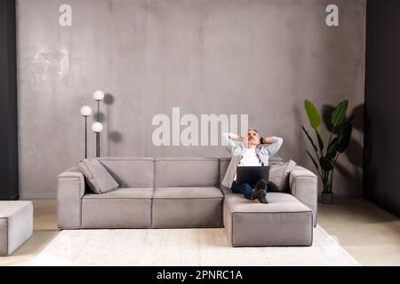 Portrait of a serious handsome bearded guy, young middle aged man in glasses is using his laptop , relaxing, lying at home on sofa couch, looking at s Stock Photo