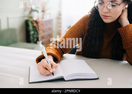Woman writing in copybook. Business woman or young female student holding pen in hand writing in paper notebook journal, taking notes studying, doing Stock Photo