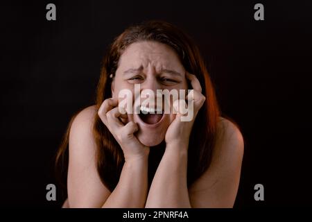 Young crying woman scratching face. Shout and scream loud with open mouth. Feelings, pain, suffering. Human emotions. Stock Photo