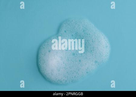 White cleanser foam bubbles on blue background or texture, close up, top view. Soap suds or foam and bubbles from detergent or shower gel or shampoo Stock Photo