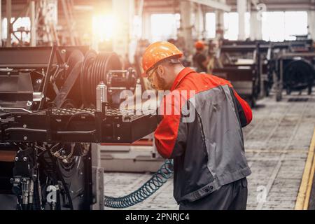Industrial worker assembles agricultural machine in workshop. Stock Photo