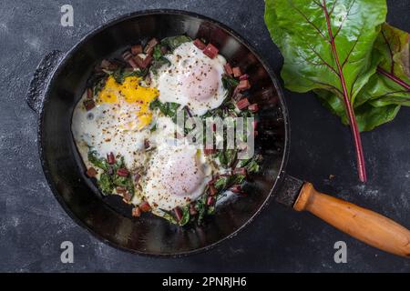 Fried eggs with green beet leaves, onion, pepper and spices in cast iron pan, close up, top view Stock Photo