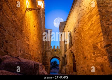 Arch in a medieval wall of the old town of Trujillo, Caceres, Spain at dusk with a full moon in the sky and night illumination Stock Photo